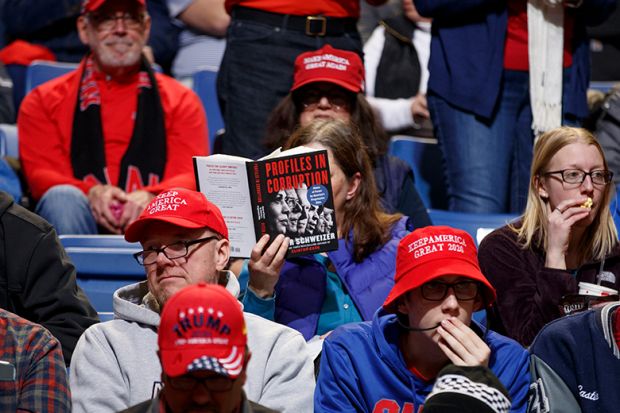 A rally attendee reads a book titled 'Profiles In Corruption', featuring 2020 Democratic presidential candidates ahead of a campaign rally for President Donald Trump. To illustrate that academic publishers are braced for a slowdown from Trump's DEI purge.