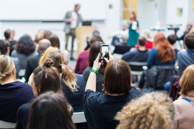 Student holding up phone in lecture. To illustrate concern about views expressed in class being shared on social media.