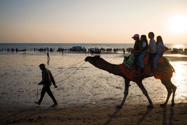 Tourists ride a camel on a beachfront in Mandvi in Gujarat, India to illustrate Coventry among India branch campus contenders