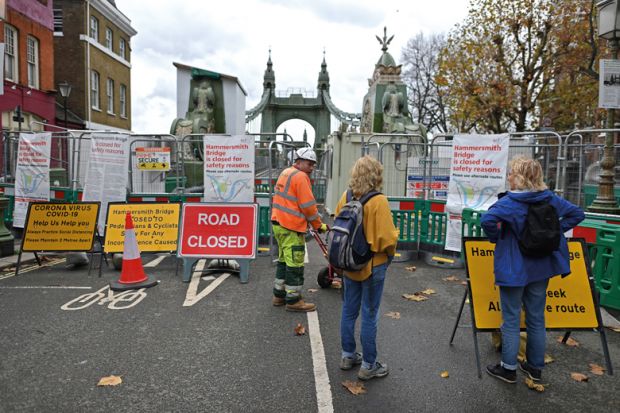 Members of the public  looking at the closed fence to the old Hammersmith Bridge over the River Thames in west London to illustrate massive closures