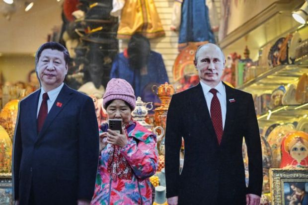 A tourist stands next to cardboard images depicting Chinese President Xi Jinping (L) and his Russian counterpart Vladimir Putin at the touristic Arbat street in downtown Moscow to illustrate Russian research is ‘increasingly isolated’ by Ukraine conflict