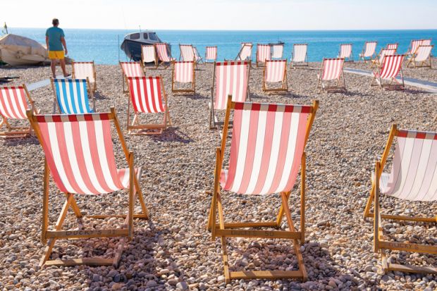 Man looking out to sea with empty deckchairs along the beach in Devon, UK to illustrate English universities battle rising tide of student no-shows