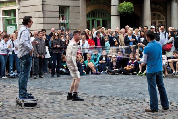 Street Entertainer unwrapping a person wrapped in cling film in Covent Garden, London to illustrate Problem of prestige dogs interdisciplinary campus