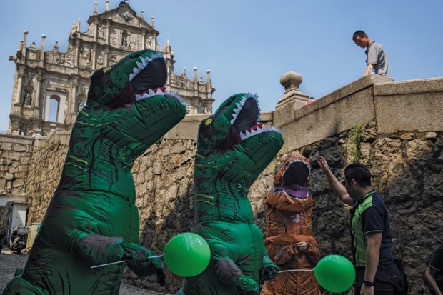 A man interacts with workers dressed in dinosaur costumes at the Ruins of St. Paul's Cathedral in Macau, China to illustrate University leaders ‘need to be better prepared for tough times’