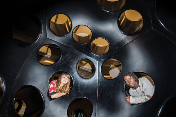 Two people looking inside holes in an immersive art installation in London, UK_to illustrate Academics urged to fill policy void at heart of new UK government