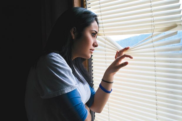 Young woman peeking through venetian blinds