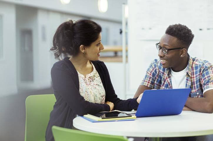 student and advisor smiling next to an open laptop